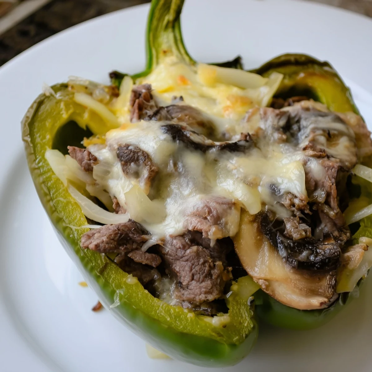 Close-up of bubbling cheese over savory beef filling inside tender Beef Philly Cheesesteak Stuffed Peppers, fresh from the oven.