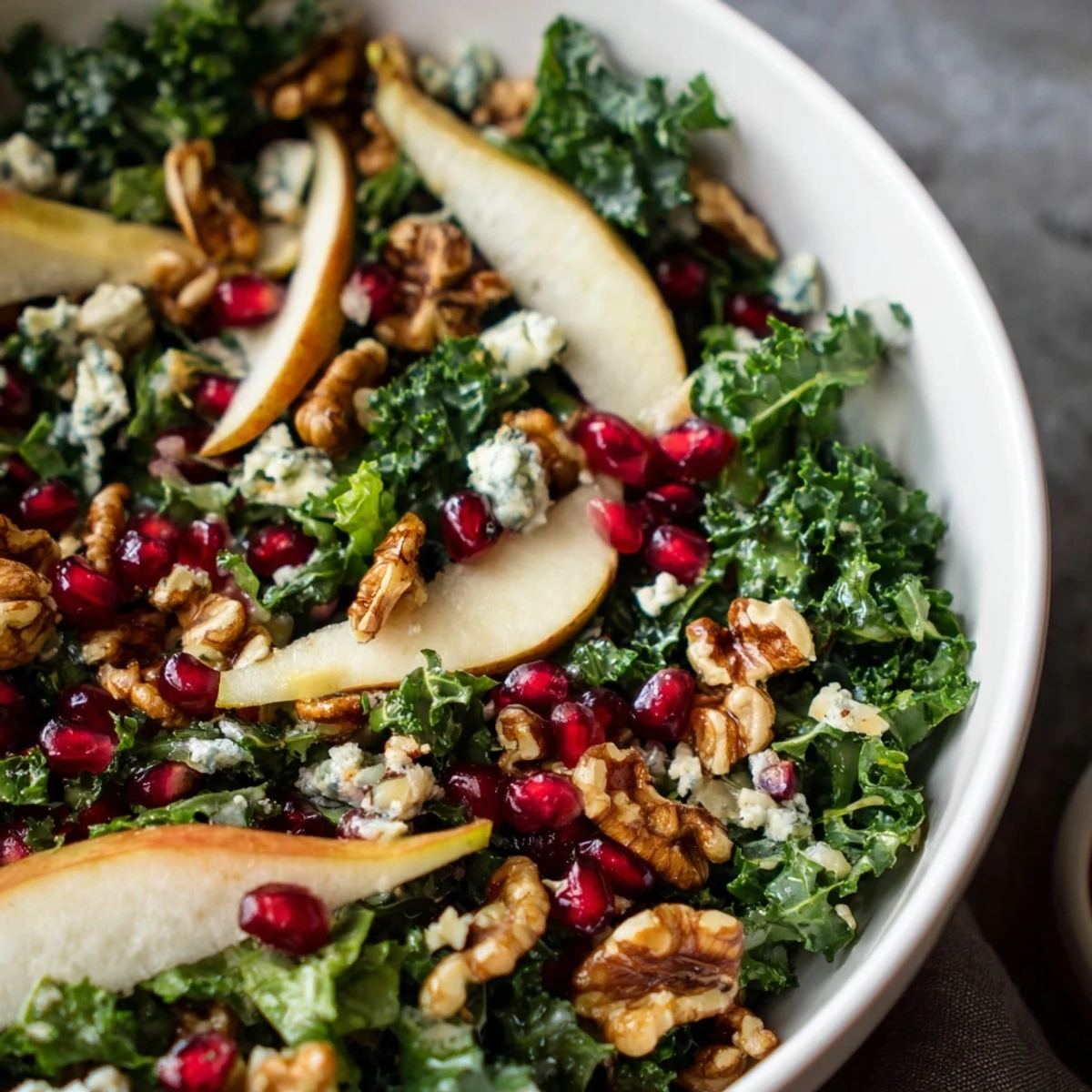 A close-up of Winter Green Salad shows crisp greens, juicy pears, crumbled blue cheese, and pomegranate seeds on a rustic table.