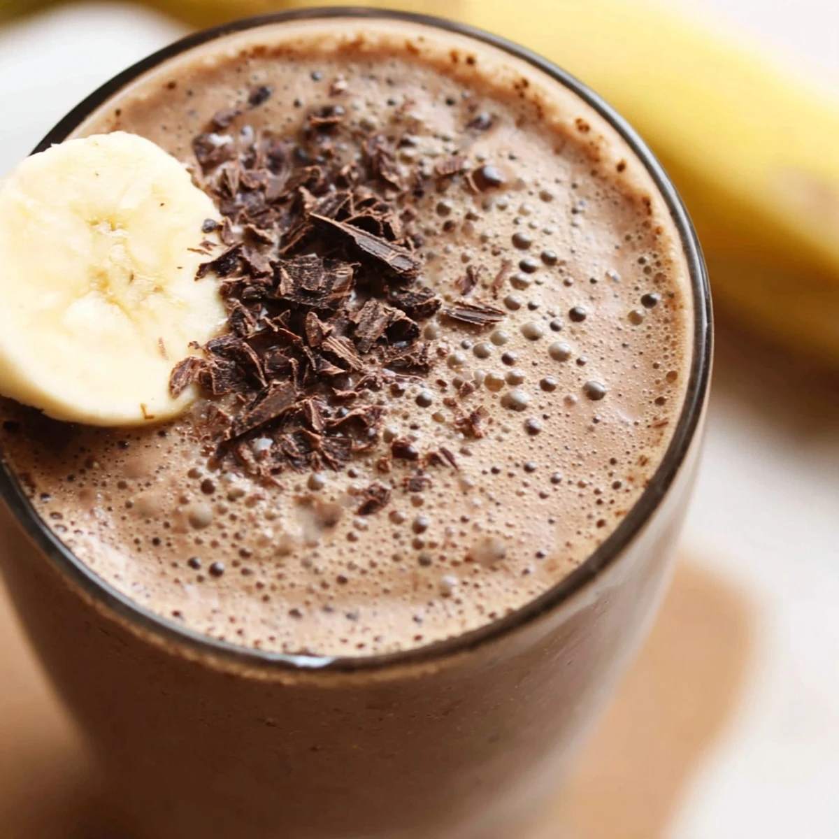 Two tall glasses of Chocolate Peanut Butter Smoothie with Banana on a wooden table, garnished with crushed peanuts and a straw.