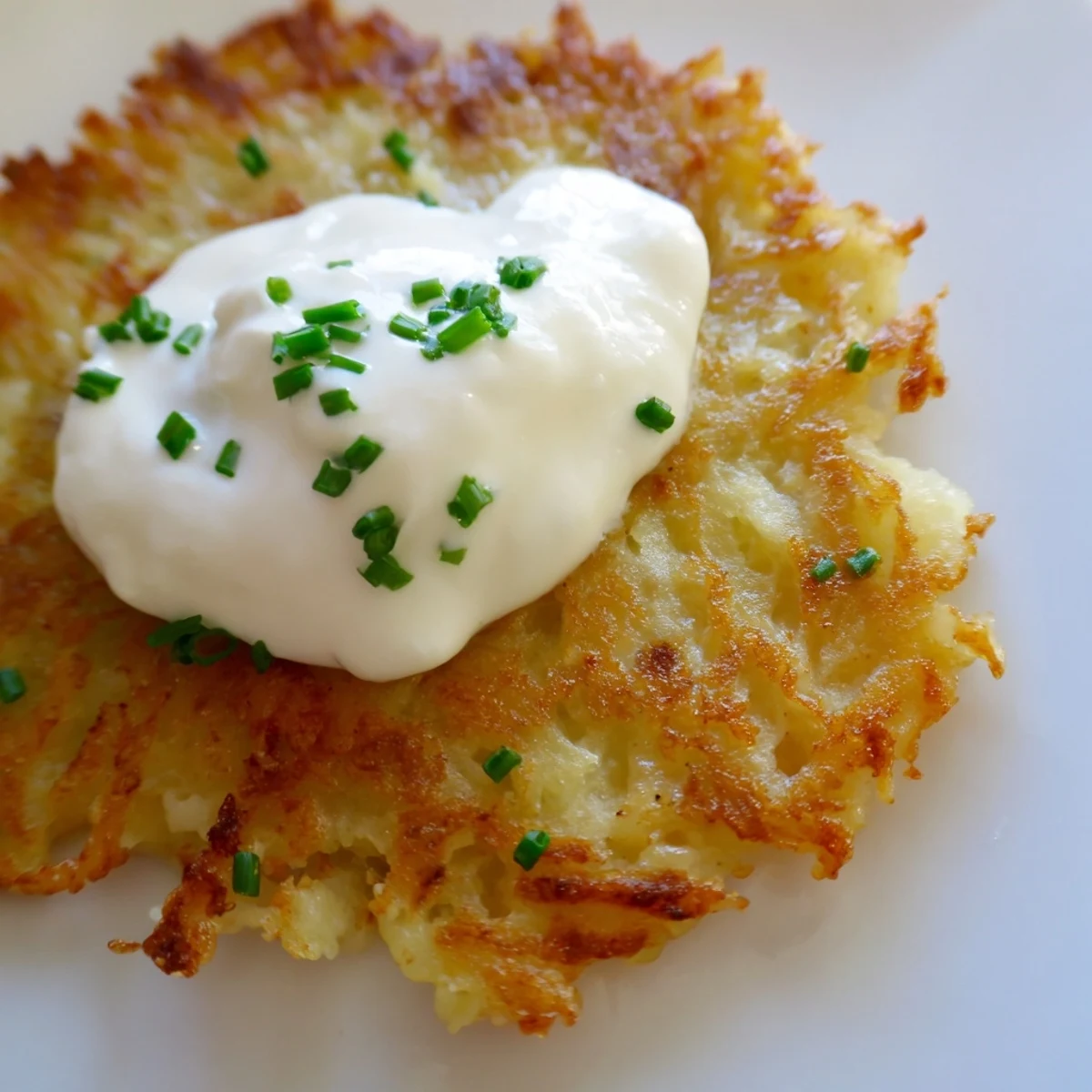 Crispy golden Irish Boxty Potato Pancakes, fried in skillet, topped with a dollop of cool sour cream and fresh chives.