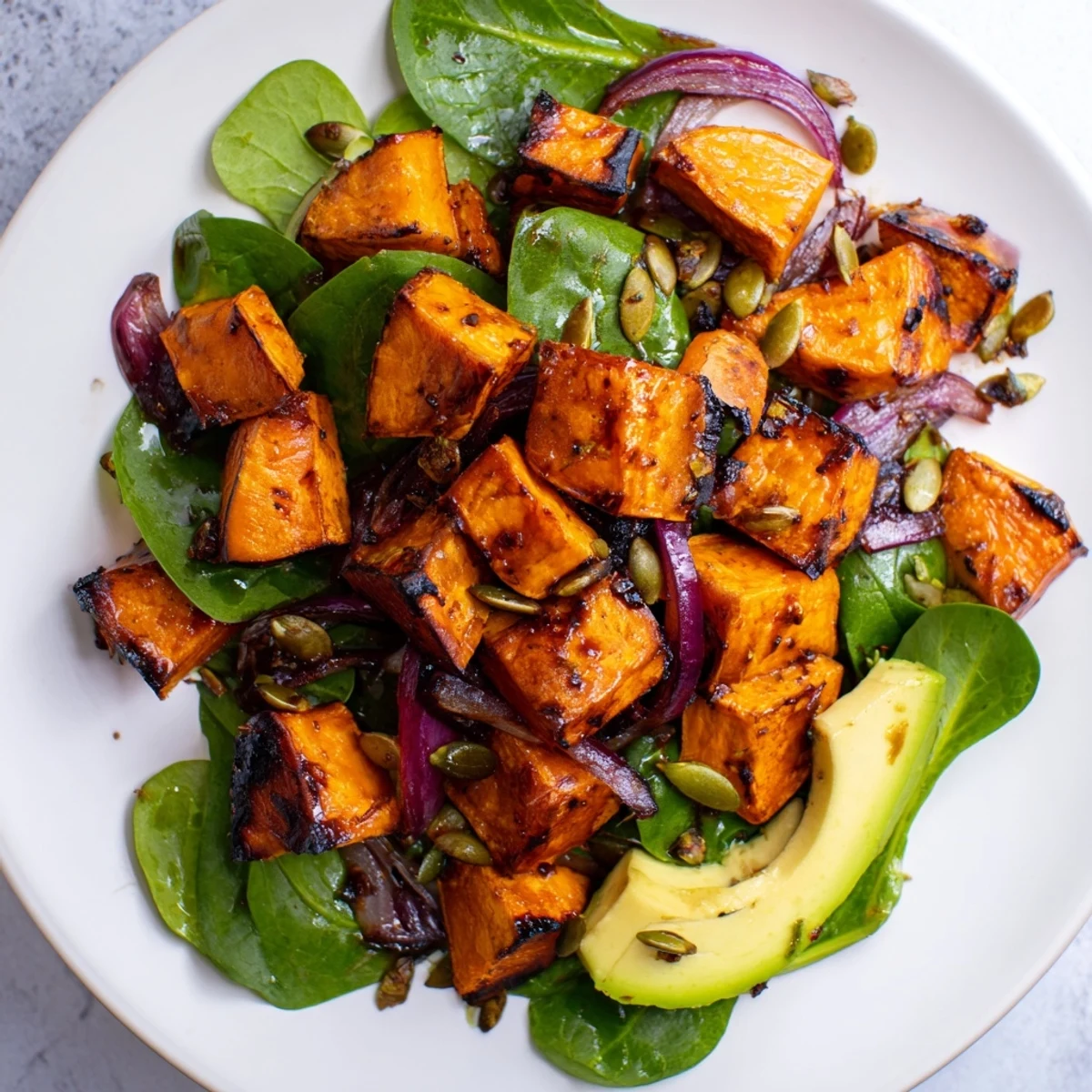 Roasted sweet potato salad with lime dressing served on a white plate, garnished with toasted pumpkin seeds and avocado, perfect for a light lunch.