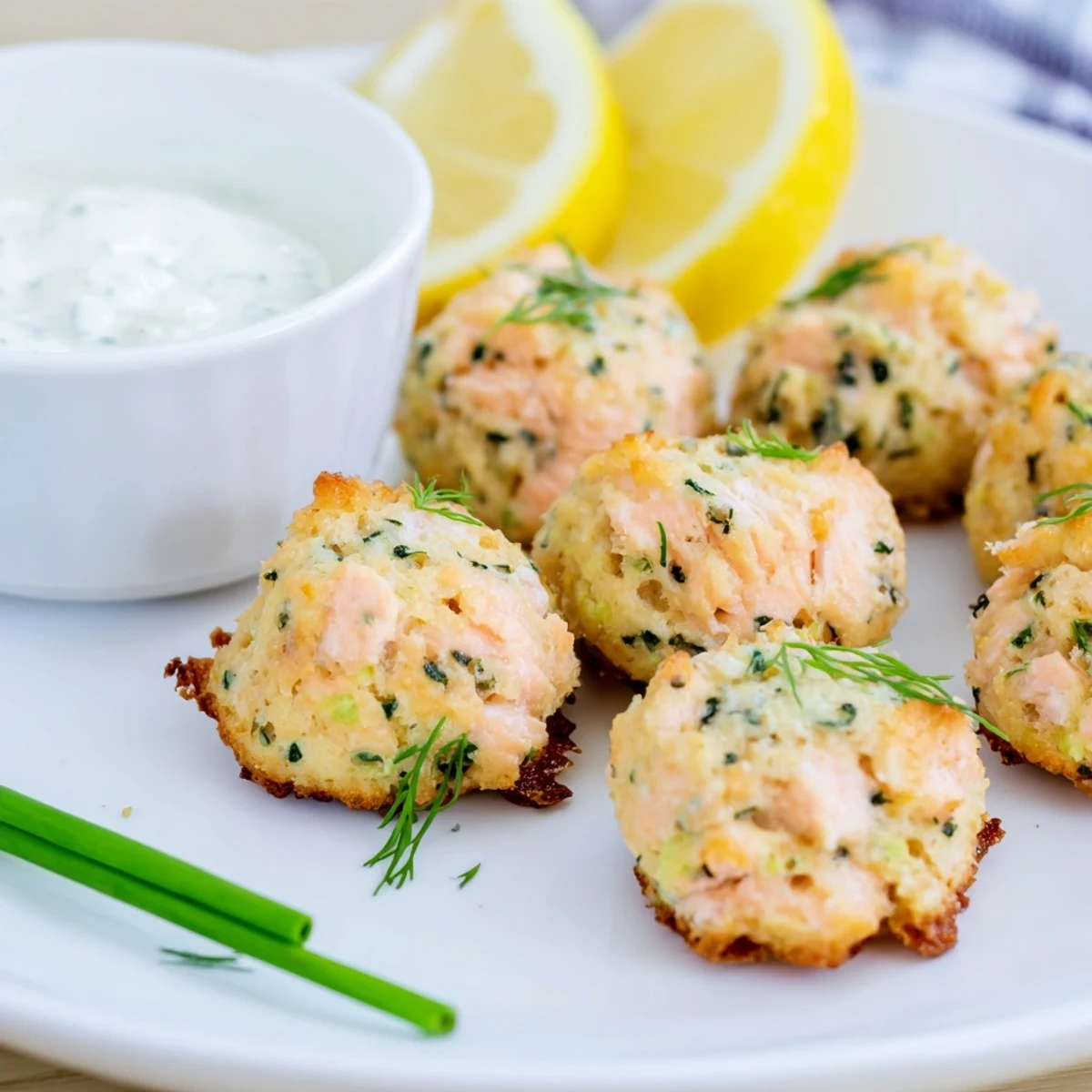 Golden-brown baked salmon snack bites arranged on a platter with lemon wedges and a creamy dip, perfect for parties.  