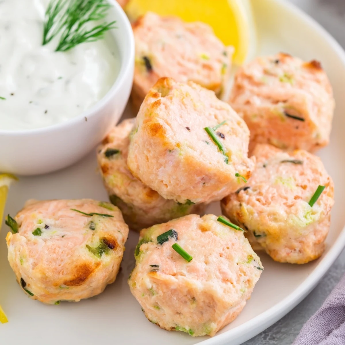Freshly baked salmon snack bites with dill and chives, served warm with a side of tangy Greek yogurt dip.  