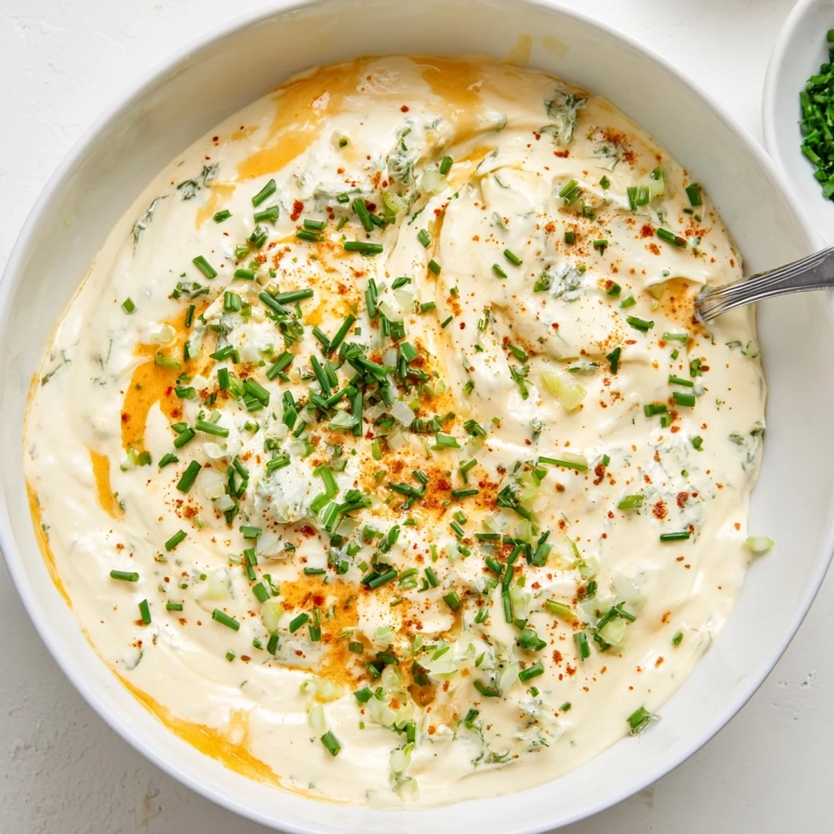 A close-up of velvety Creamy Snack Cheese Dip topped with chopped chives, surrounded by colorful sliced cucumbers, carrots, and bell pepper strips.  