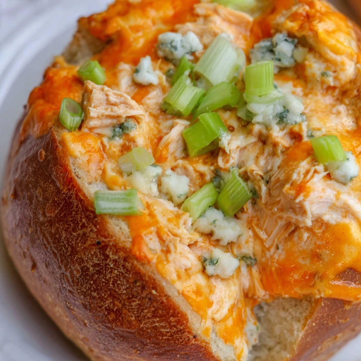 Freshly baked Tailgate Buffalo Chicken Dip bubbling inside a hollowed sourdough bread bowl, served with celery and carrot sticks. 