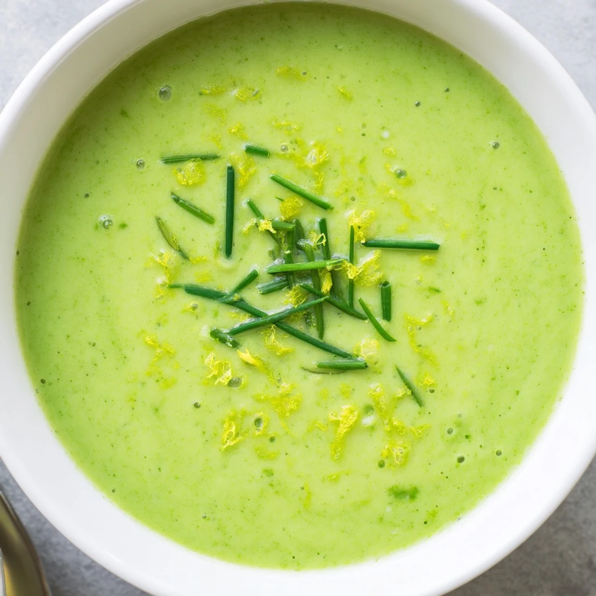 Steaming bowl of Creamy Asparagus Soup with Lemon, garnished with fresh chives and a swirl of cream.