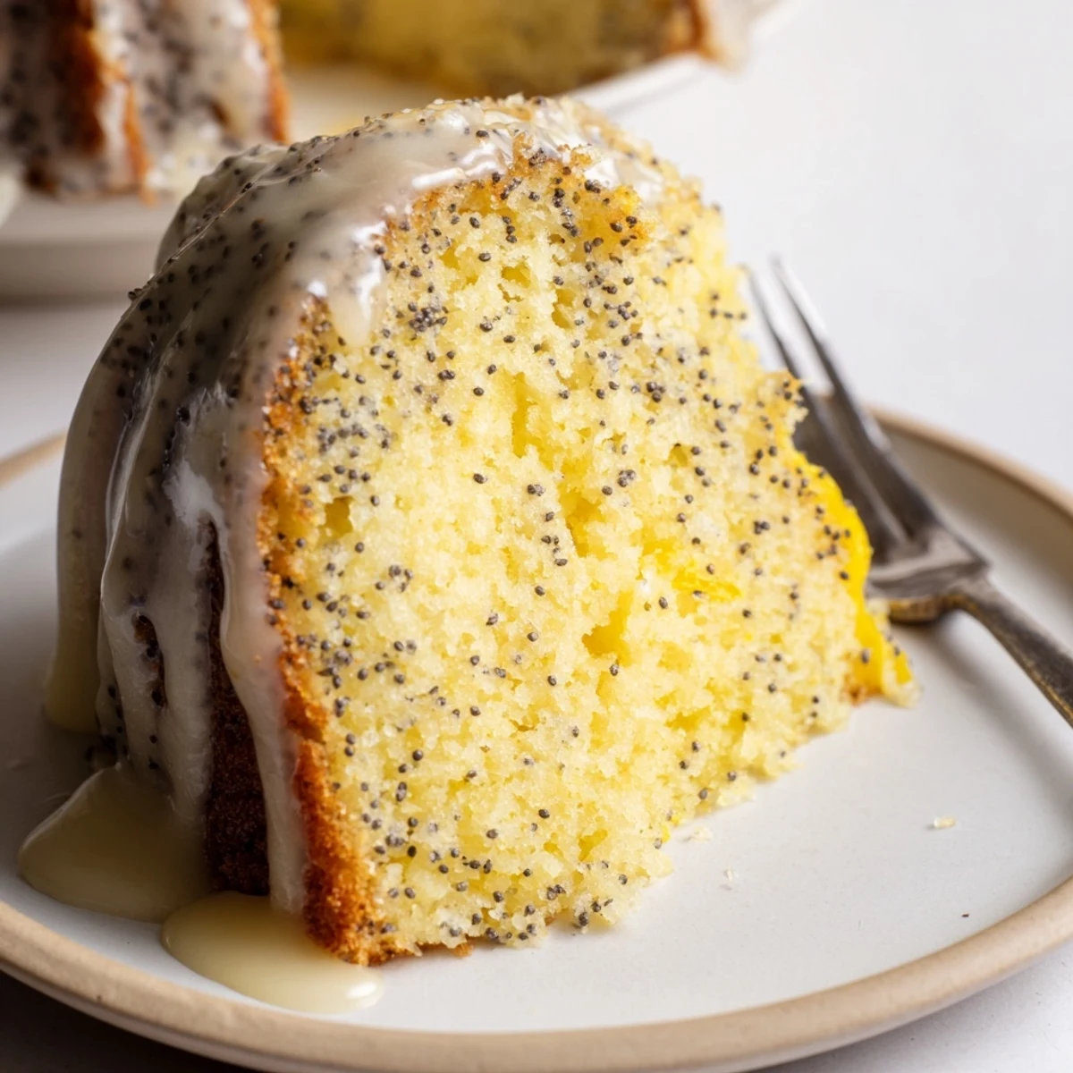 A glazed Lemon Poppy Seed Bundt cake sits on a marble counter, showcasing its tender crumb and golden-brown ridges.  
