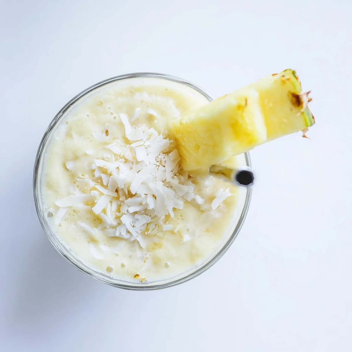 Pouring the vibrant Pineapple Coconut Smoothie into a clear glass, topped with shredded coconut and a bright pineapple slice, perfect for warm afternoons.