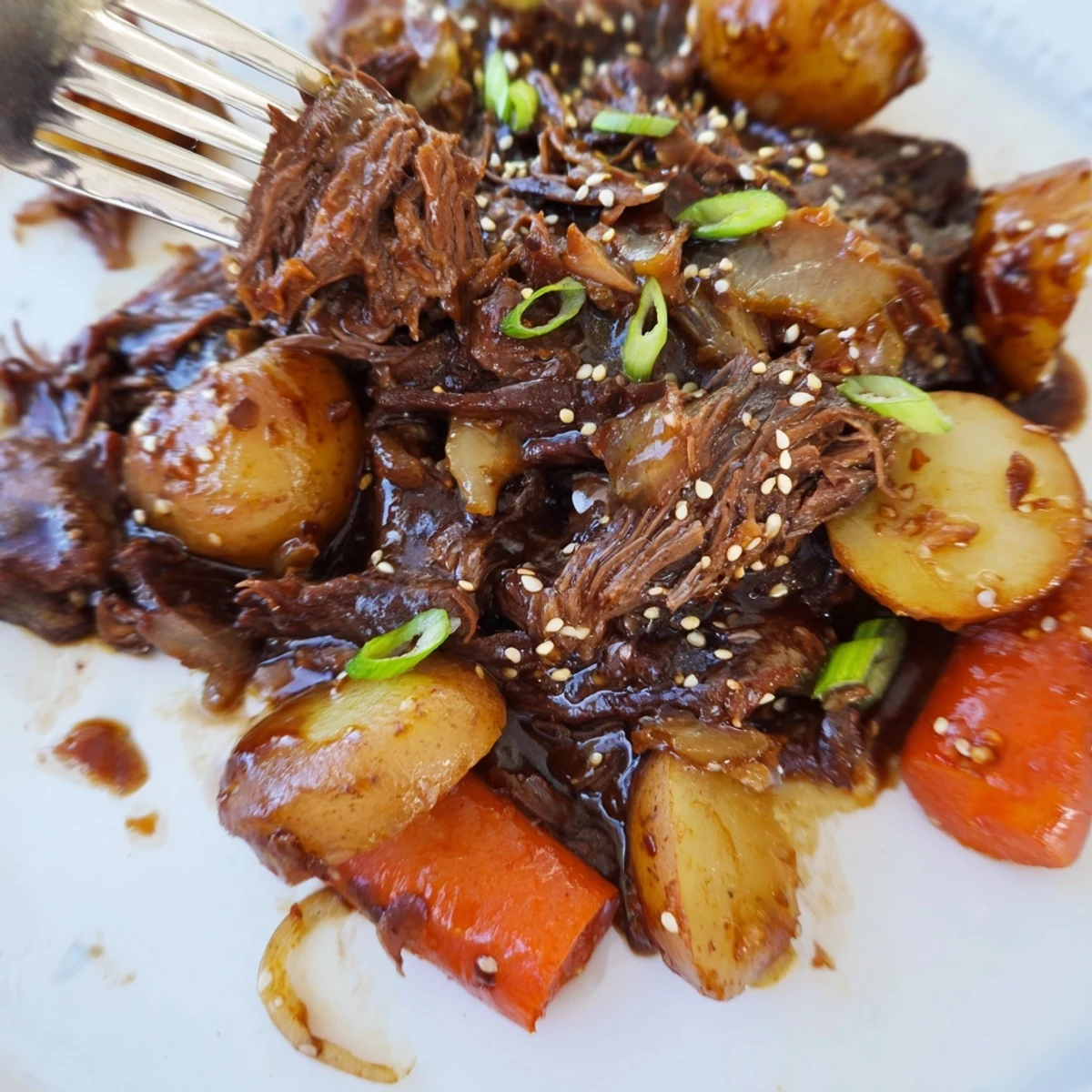 Tender slow cooker Korean beef pot roast falling apart over carrots and potatoes, drizzled with soy garlic gravy.