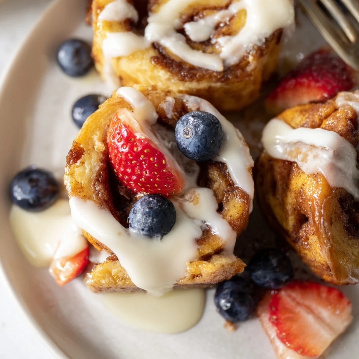 Cinnamon Roll French Toast Bites being dipped in an egg mixture, cooked to a perfect custardy interior in a skillet for a cozy brunch.