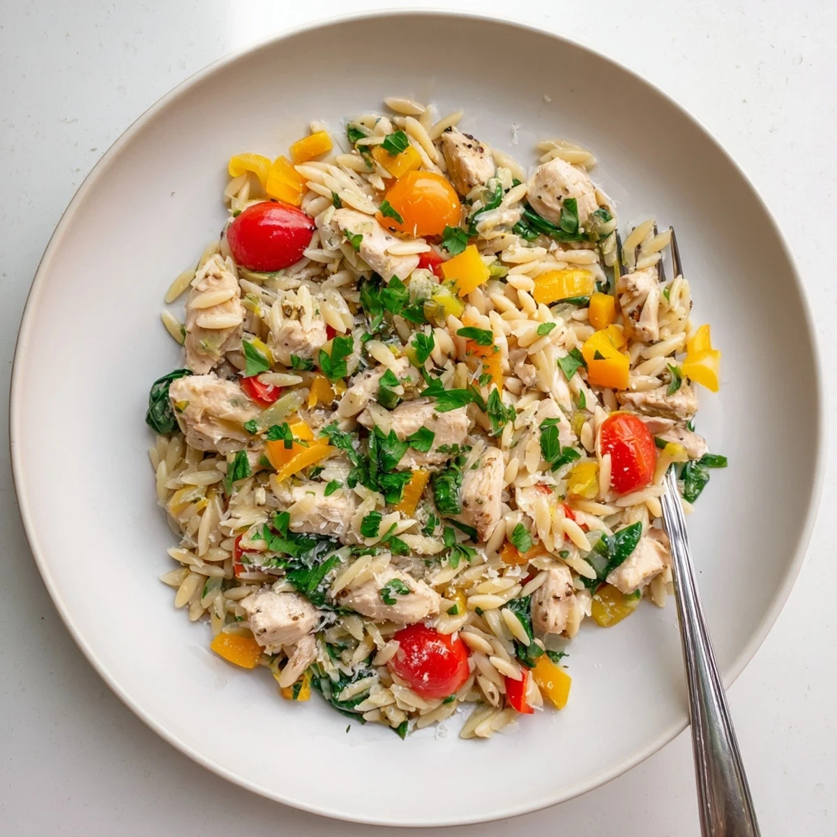Serving suggestion for High Protein Chicken Orzo plated in a white bowl with a lemon wedge and fresh parsley garnish.