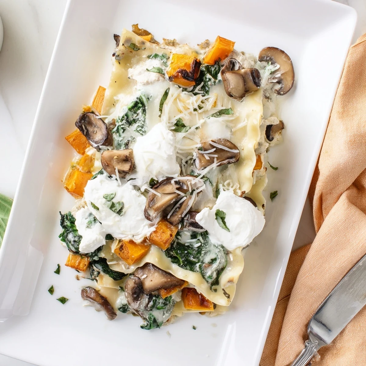 Close-up of Butternut Squash, Spinach & Mushroom Lasagna with bubbly cheese crust and fresh spinach peeking through.