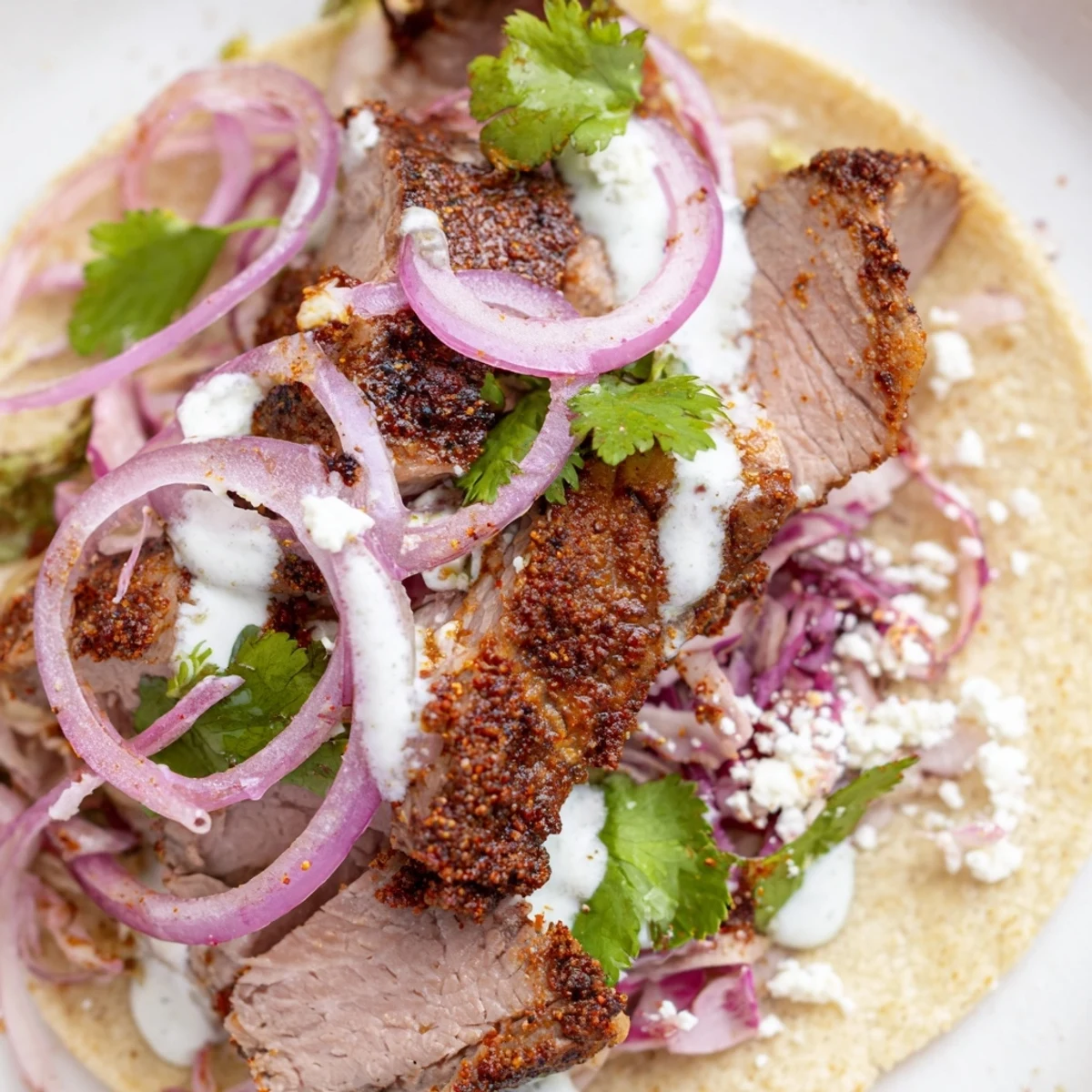 Close-up of cumin crusted leg of lamb nestled in soft tortillas, drizzled with yogurt-lime sauce and topped with cheese.