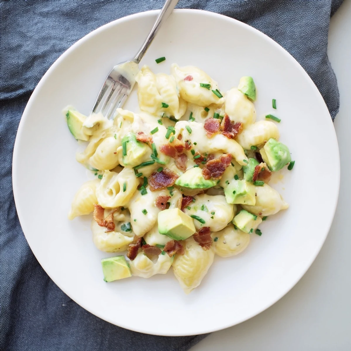 Family-style serving of avocado and bacon mac and cheese with melted cheese sauce and a squeeze of lemon.