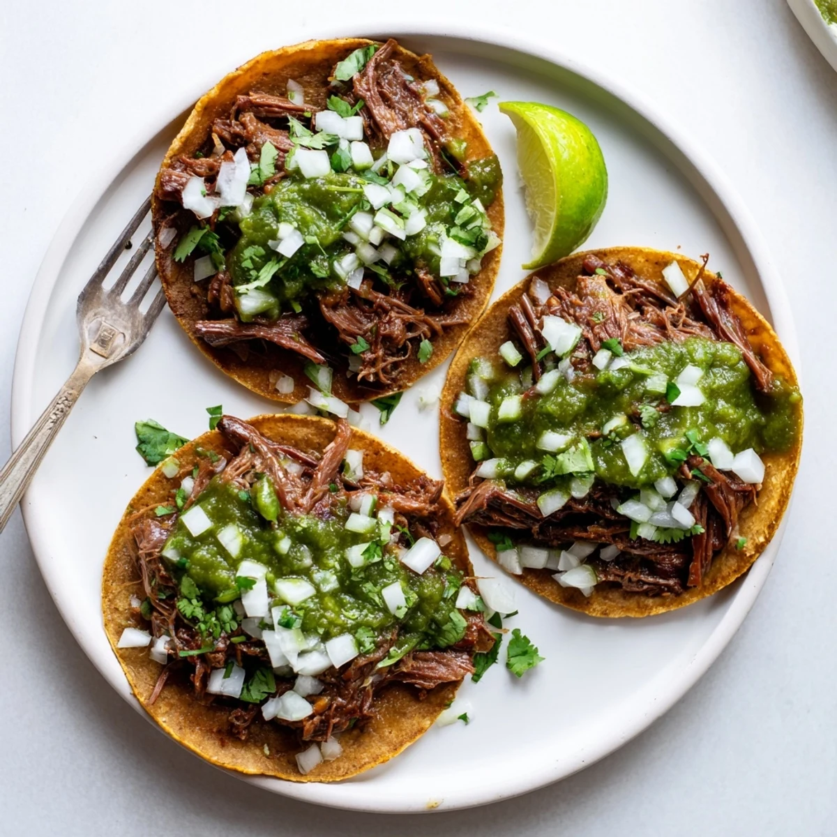 A close-up of juicy Beef Cheek Tacos filled with shredded meat, fresh cilantro, onions, and vibrant salsa verde.