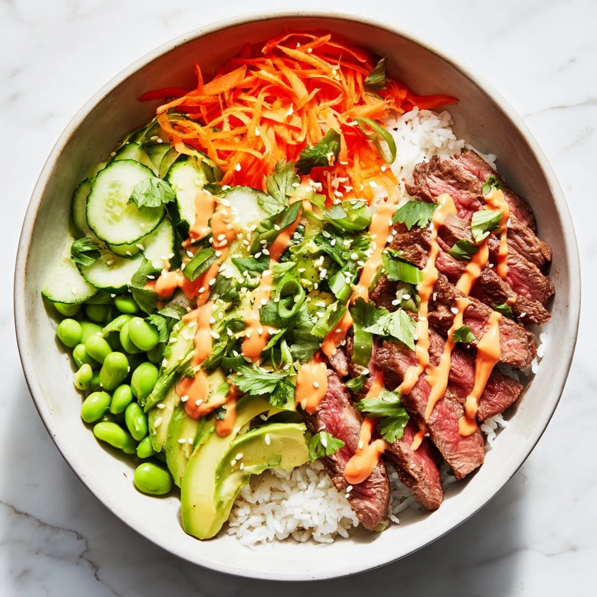 Colorful flank steak bowl featuring tender beef edamame carrots cucumbers and creamy Sriracha drizzle