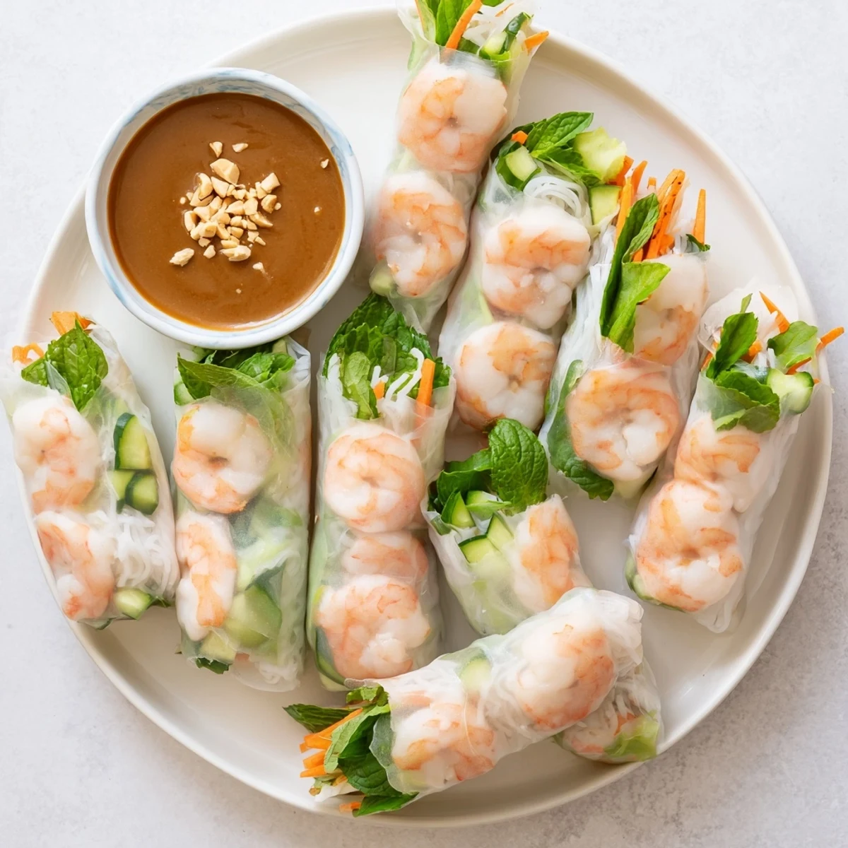Light and fresh Vietnamese spring rolls arranged on a serving platter with crisp julienned carrots, cucumber, mint and creamy peanut dipping sauce