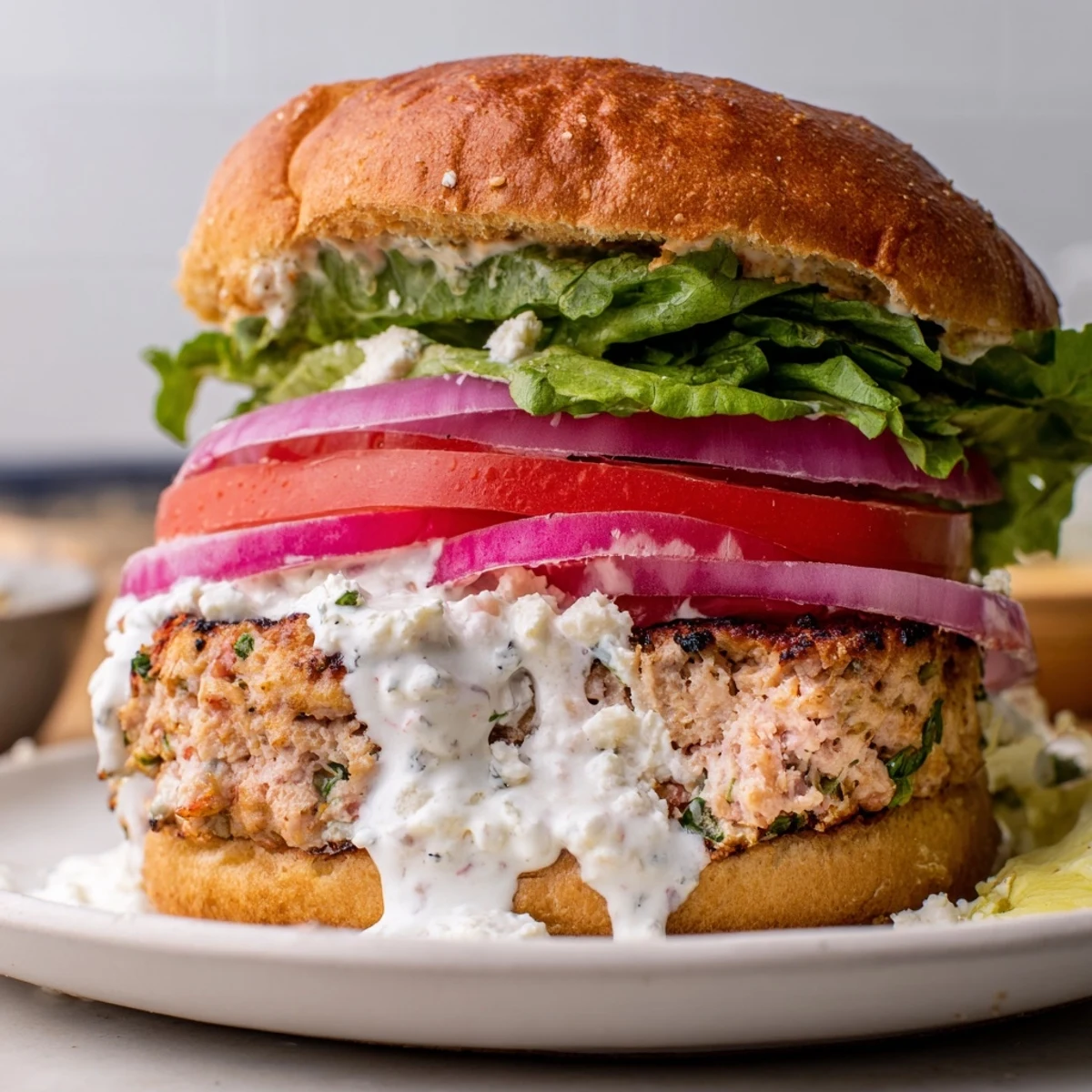 Golden brown Greek chicken burgers topped with fresh vegetables and creamy tzatziki sauce on toasted buns