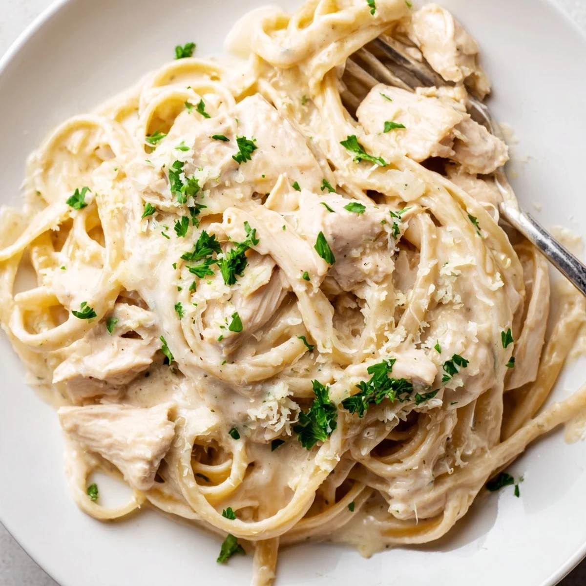Golden chicken breasts simmering in crock pot with garlic cream sauce and fettuccine