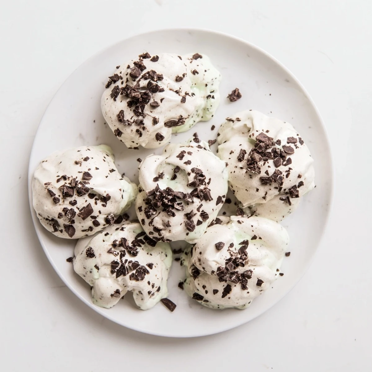 Airy chocolate meringue cookies studded with mint chips on parchment-lined baking sheet