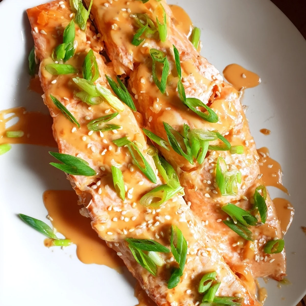 Flaky Bang Bang Salmon pieces coated in rich mayonnaise sauce served on white plate