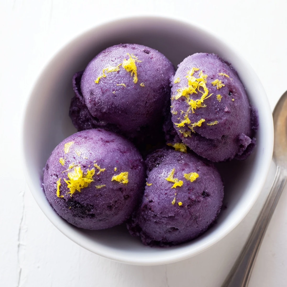 Vibrant blueberry lemon sorbet being scooped from a loaf pan with metal ice cream scoop