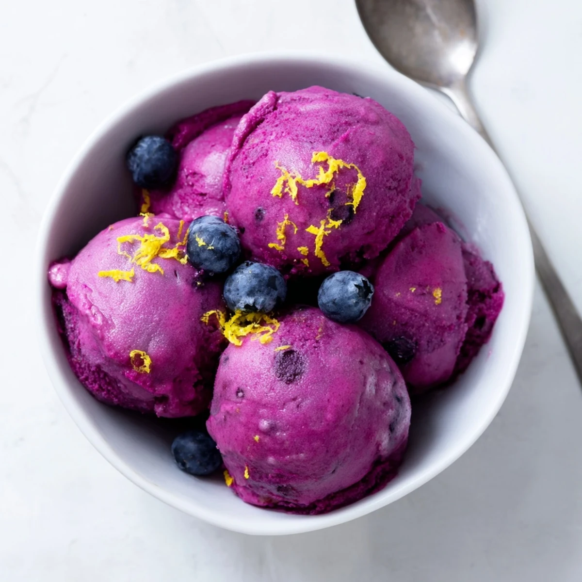 Creamy dairy-free blueberry lemon sorbet mounded in a white serving dish with lemon zest