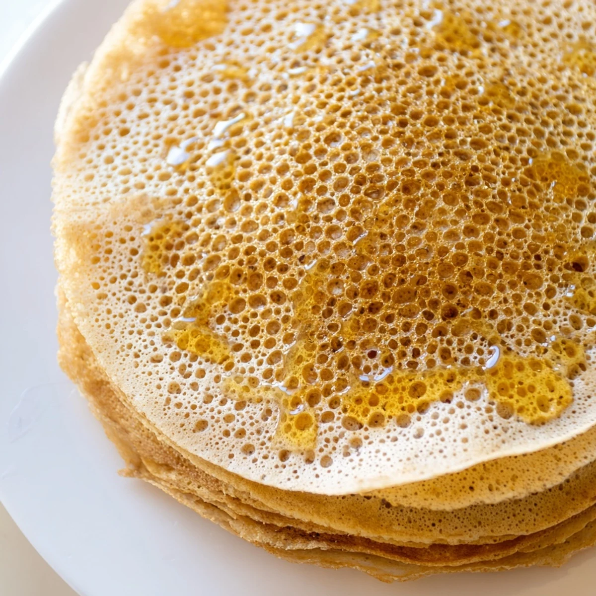 Light spongy baghrir cooking in a skillet showing signature tiny holes across the surface