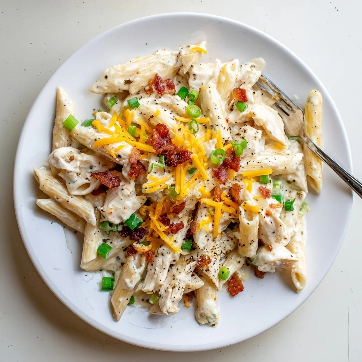 Creamy crack chicken pasta topped with crispy bacon and melted cheddar cheese in a rich white sauce