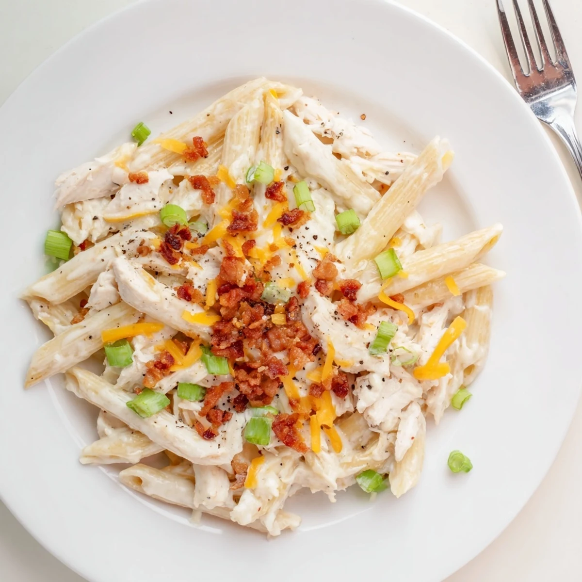 Twirl of penne pasta coated in cheesy crack chicken sauce with bacon bits and black pepper garnish