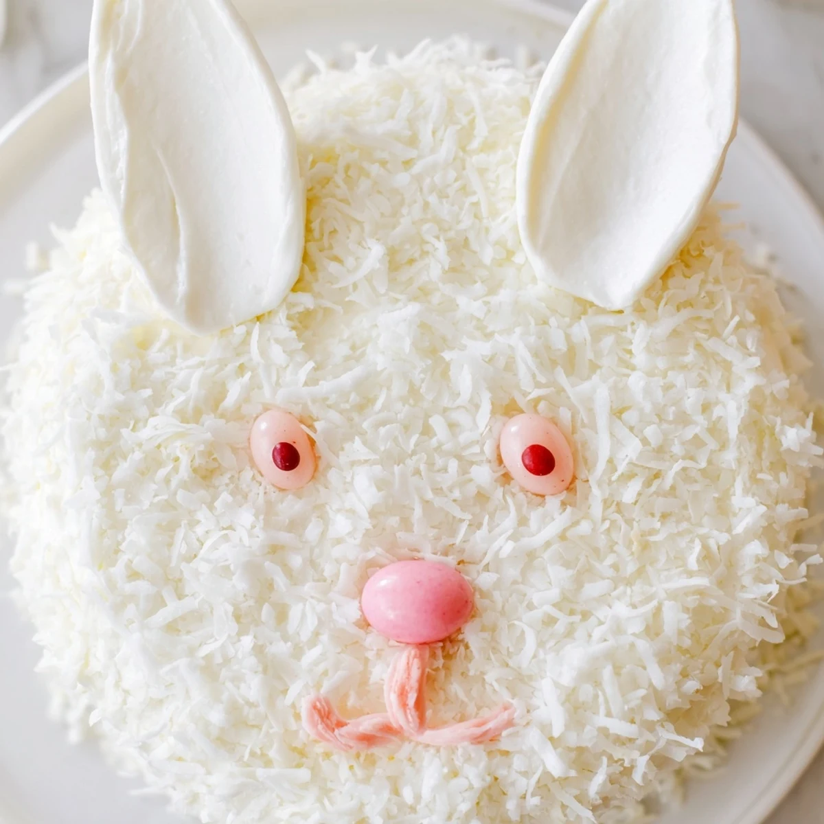 Adorable white bunny cake with fluffy coconut fur and pink candy details on serving platter