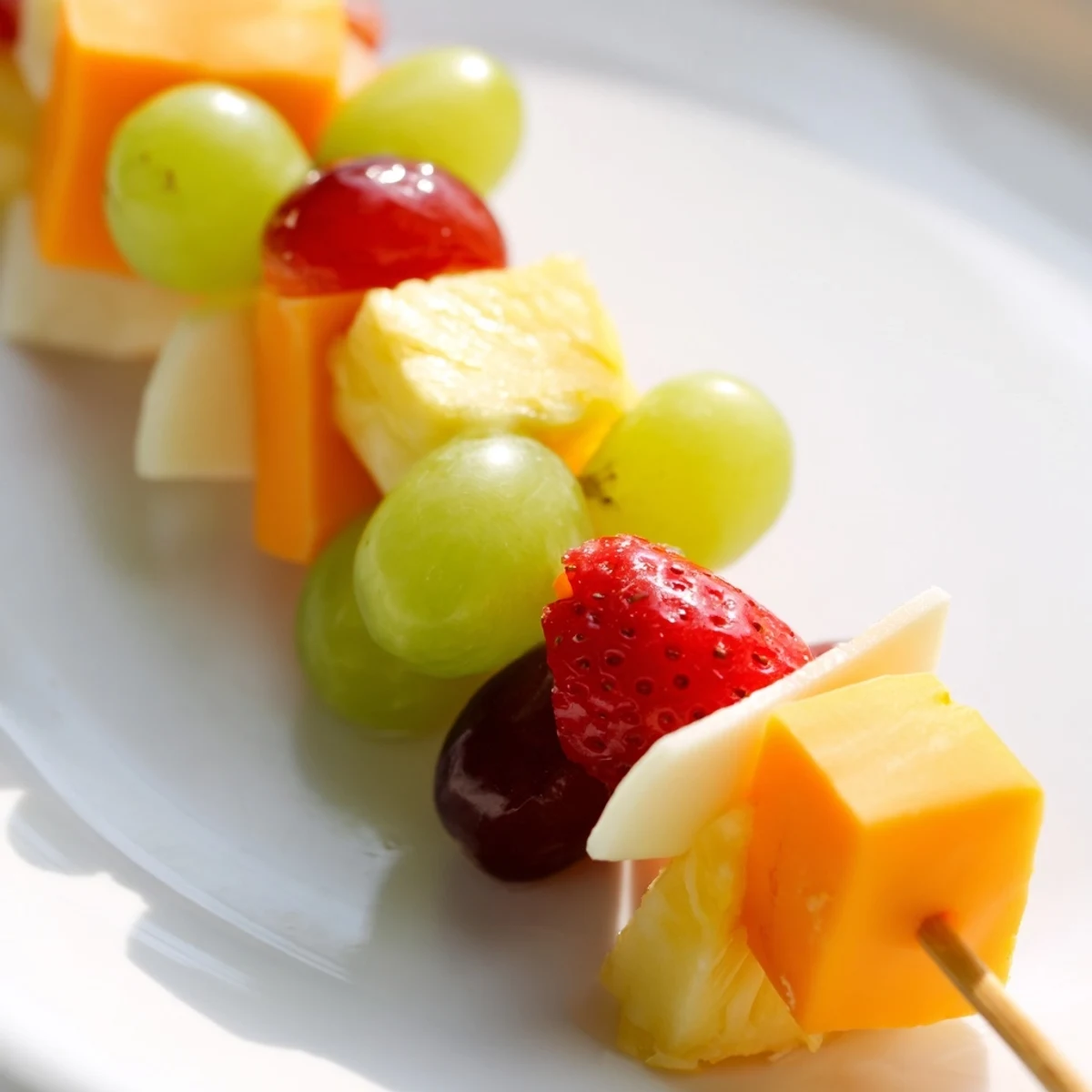 Colorful fruit and cheese kabobs arranged on a platter with grapes strawberries and cheddar cubes