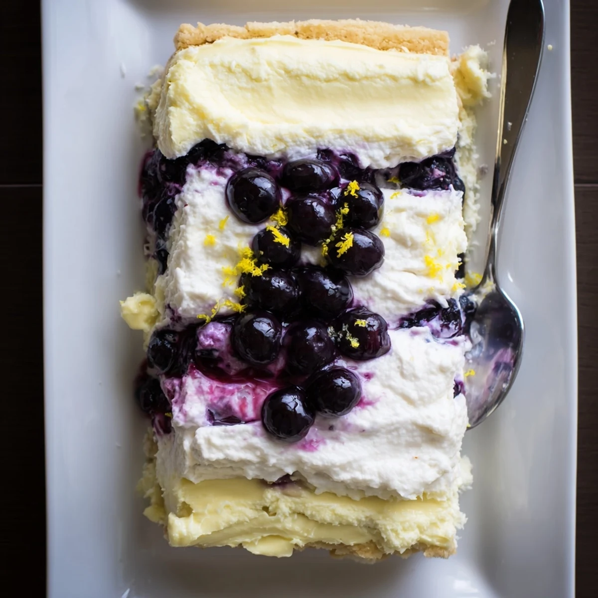 Thick slices of lemon blueberry lasagna layered with purple berry sauce and whipped cream