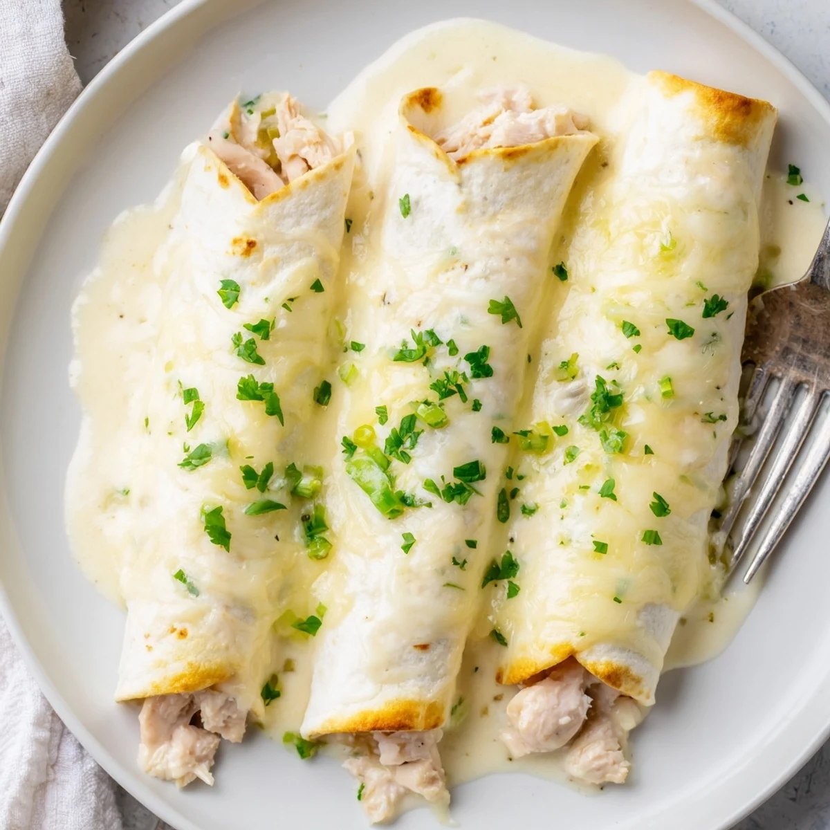 White Rotisserie Chicken Enchiladas bubbling in creamy white sauce, golden melted cheese