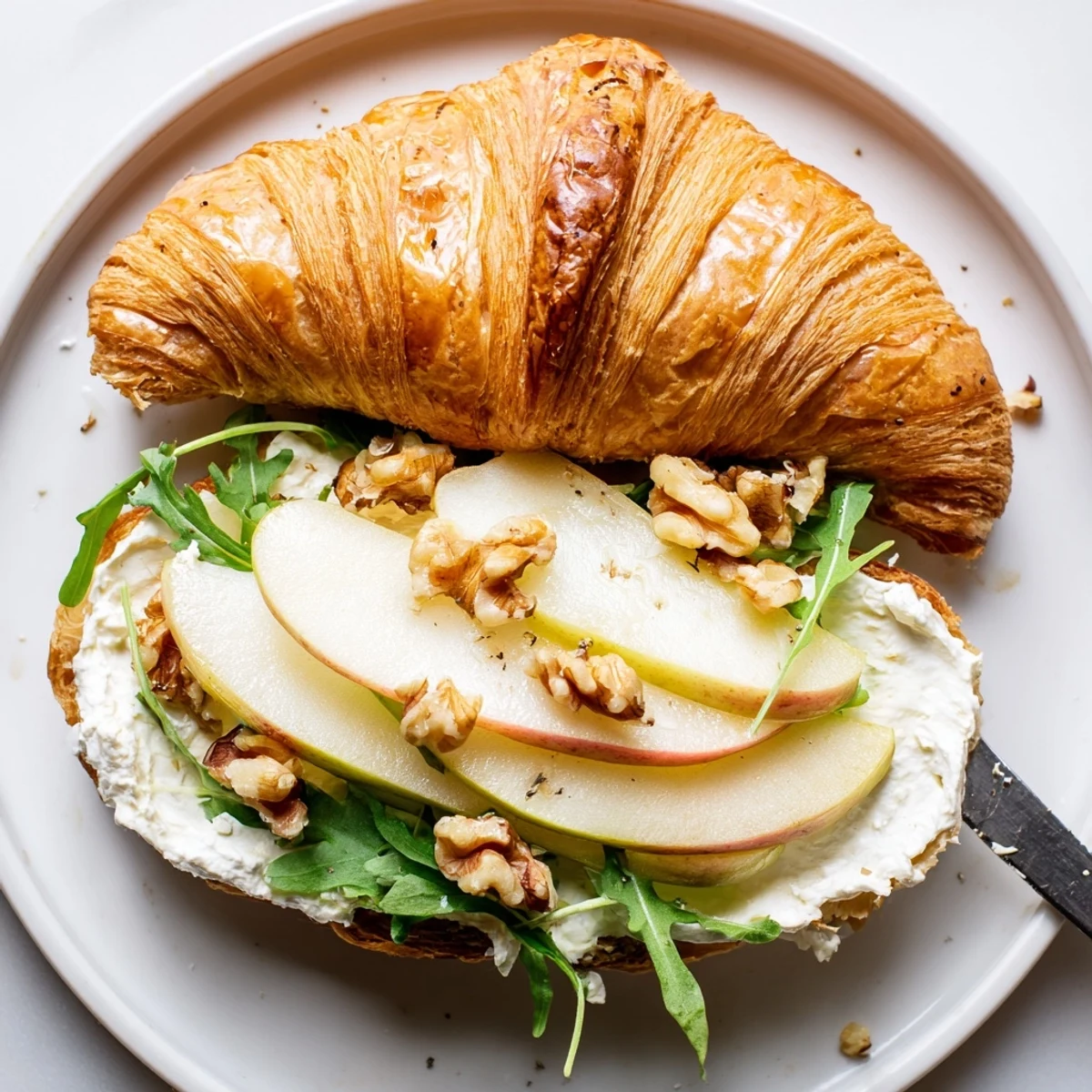 A lightly toasted Apple Goat Cheese Croissant Sandwich served with honey drizzle