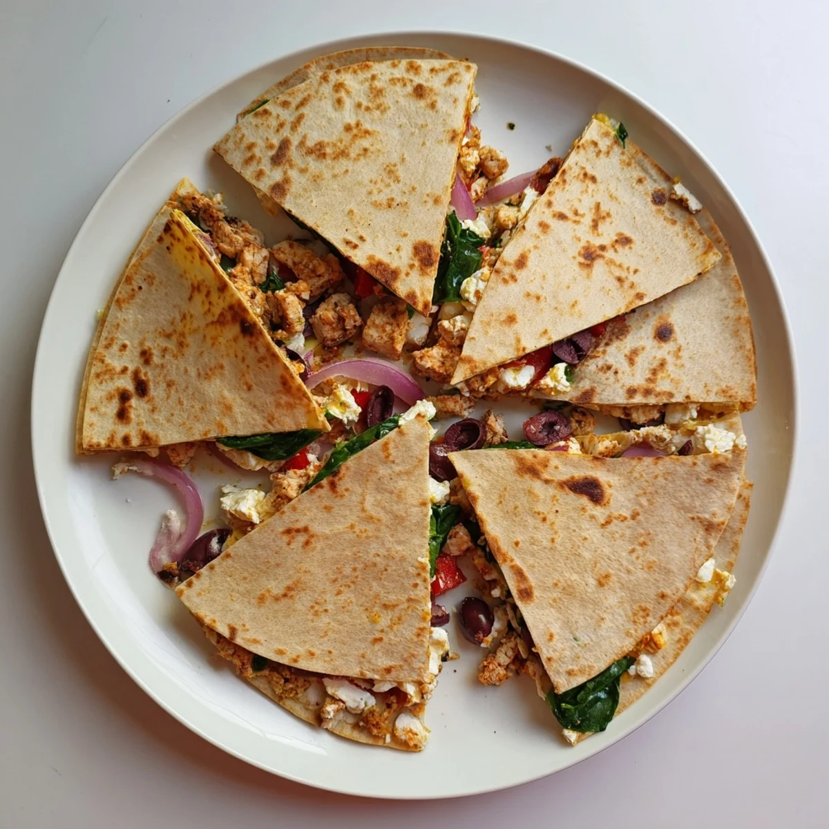 Pan-fried quesadilla featuring seasoned chicken breast topped with spinach and crumbled feta cheese on a serving platter