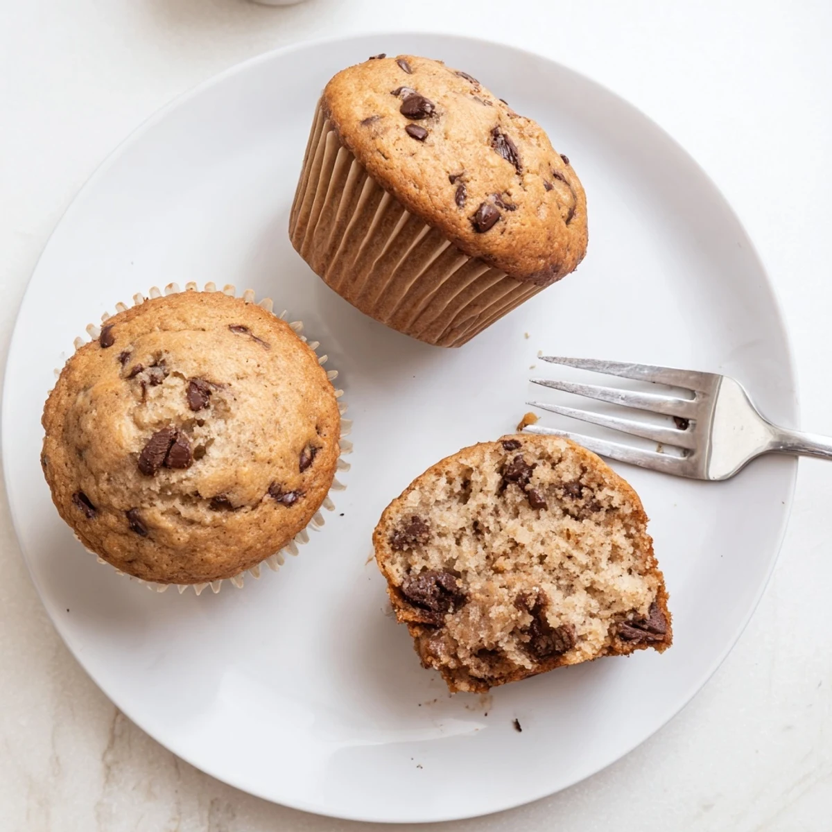 A batch of twelve fluffy banana chocolate chip muffins cooling on a wire rack, ready for breakfast