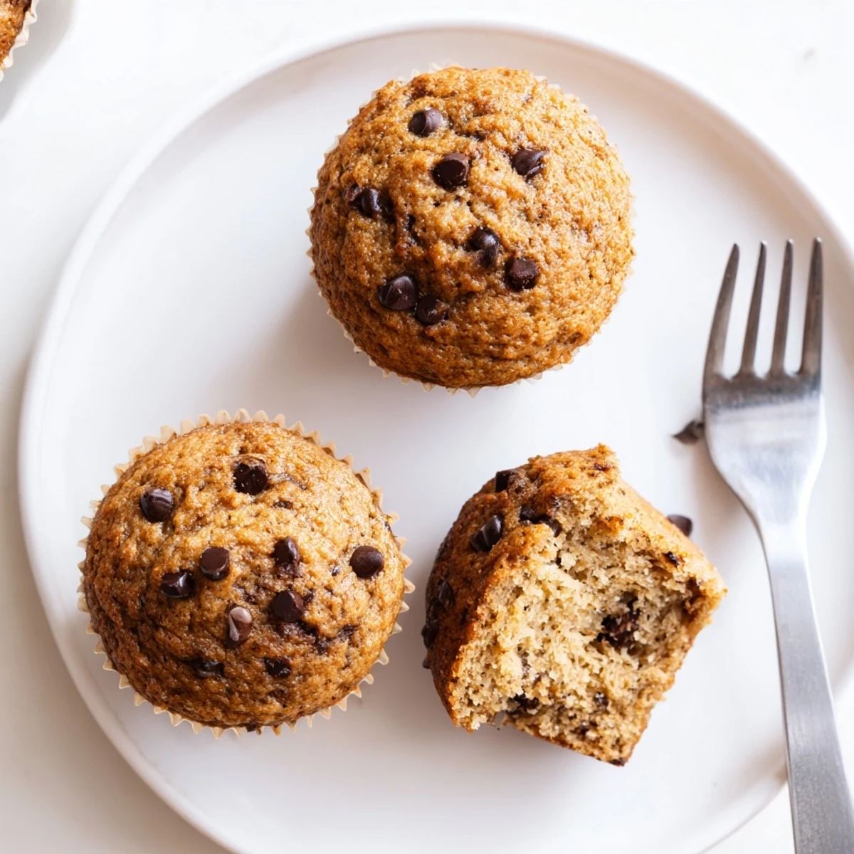 Warm homemade banana chocolate chip muffins stacked on a wooden serving board, showcasing their tender texture and rich chocolate swirls