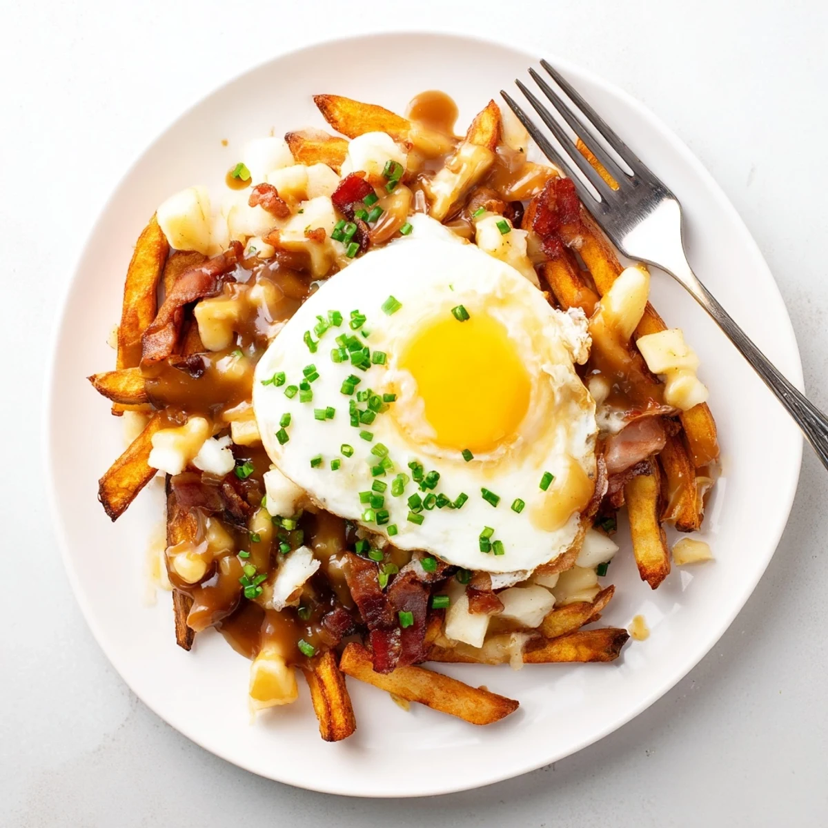 Hearty ultimate breakfast poutine featuring smoky bacon, fried eggs, and savory beef gravy over potato fries
