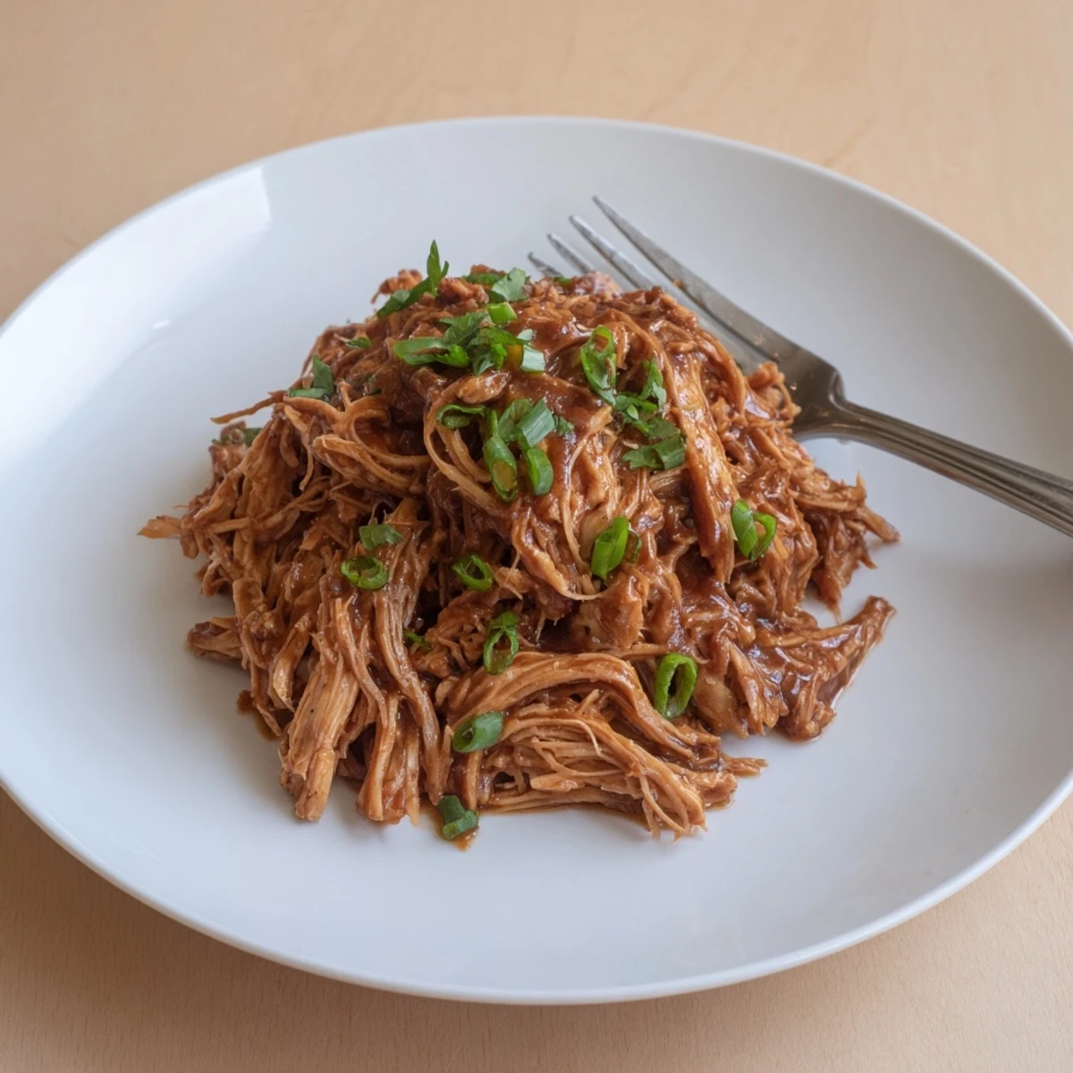 Slow Cooker Brown Sugar Garlic Chicken shredded on plate, sticky sweet sauce.