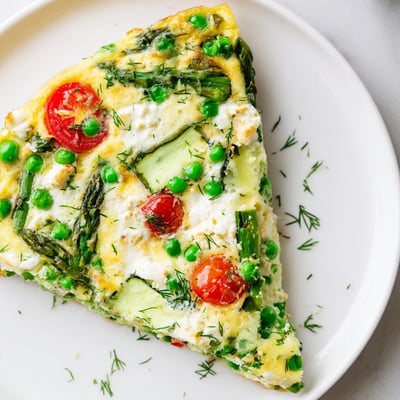 A close-up of Spring Vegetable Frittata with Herbs reveals colorful zucchini, peas, and cherry tomatoes nestled in a golden egg base.